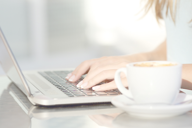 Detalle de las manos de una profesional del marketing digital que escribe en un ordenador portátil con una taza a su lado.